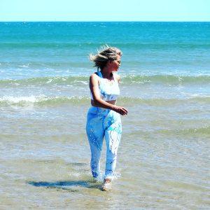 Blond woman walking in shallow water with leggings and a swim bra from Mantaraj. Beautiful sustainable active wear.