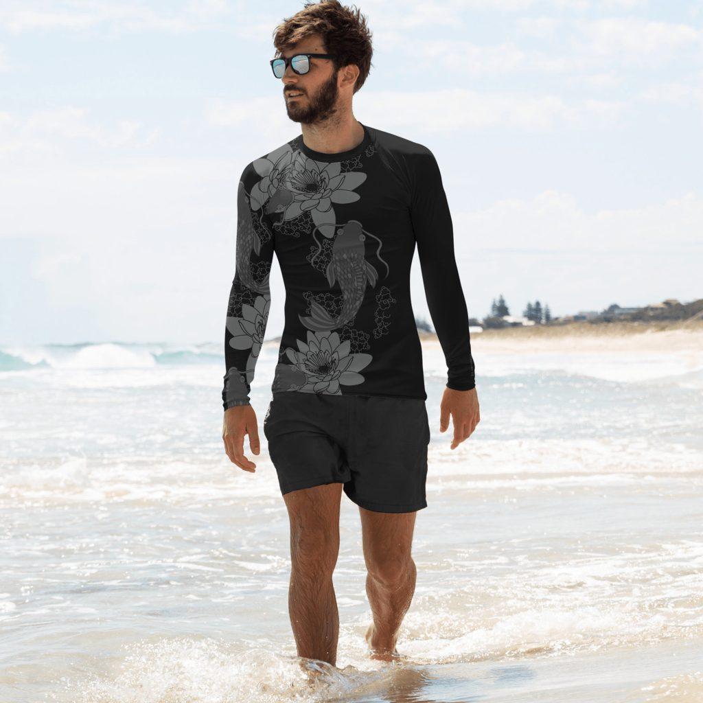 Man walking on a beach with the feet in the water with sunglasses and a black swim shirt from Mantaraj with water lilies